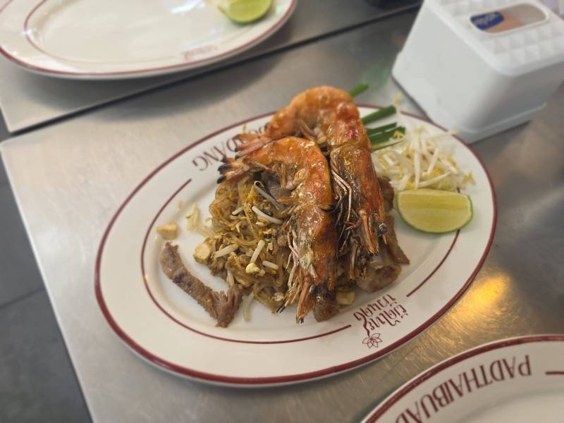 ผัดไทยกุ้งแม่น้ำบนจานโลโก้ร้าน พร้อมถั่วงอกและมะนาว